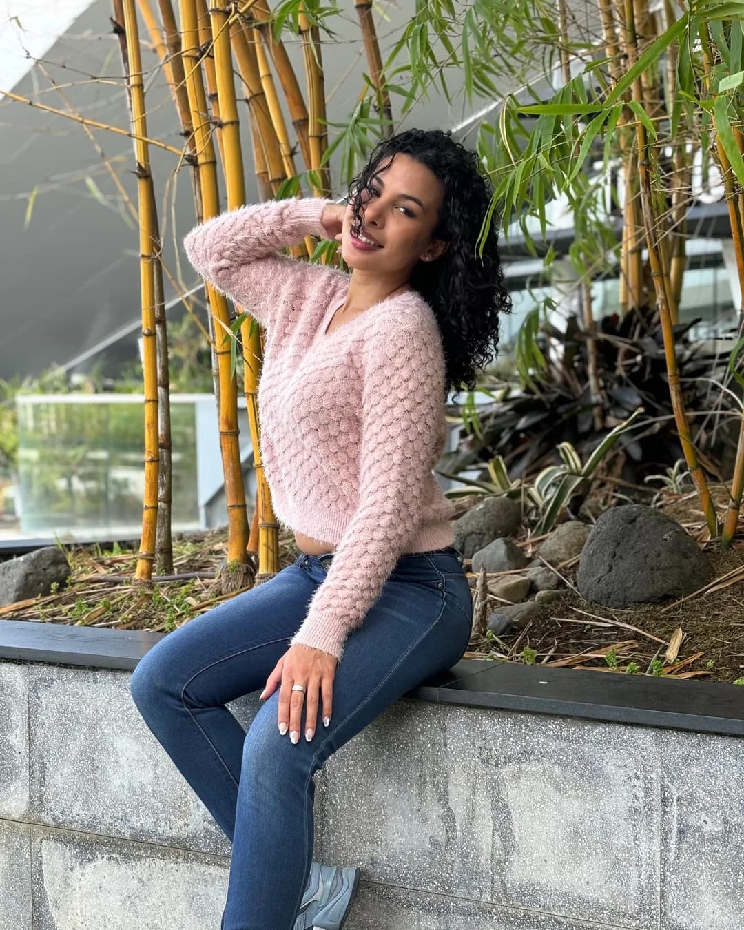 Woman in a blush popcorn-knit sweater sitting on a garden wall